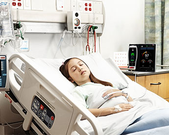 Patient im Krankenhausbett, der einen Masimo-Sensor trägt, mit einem Root-Gerät im Hintergrund.