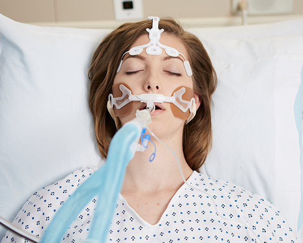 Schlafender intubierter Patient in einem Krankenhauskittel wird mit einem Masimo-Stirnsensor überwacht.